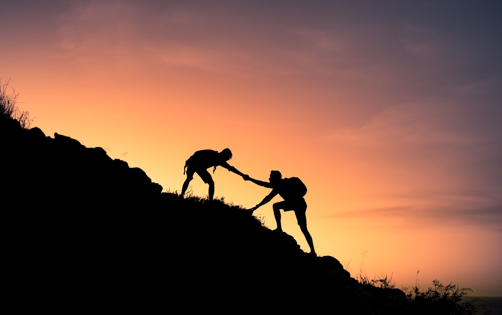 A person helping another person up a hill in the sunset